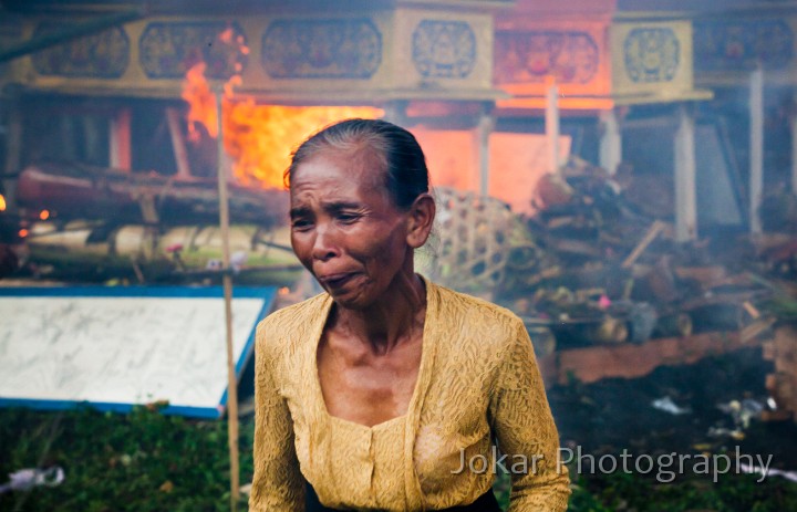 Bangli_cremation_20100829_144.jpg - 10. BANGLI CREMATION #2 - A member of the cremation congregation winces in discomfort after depositing some last offerings onto the hot smoky funeral pyre. She isn’t ‘mourning’ – Balinese cremations are generally joyous, even boisterous, occasions intended to both encourage and celebrate the release of the soul from the confines of the body. Bunut, Bangli Regency.